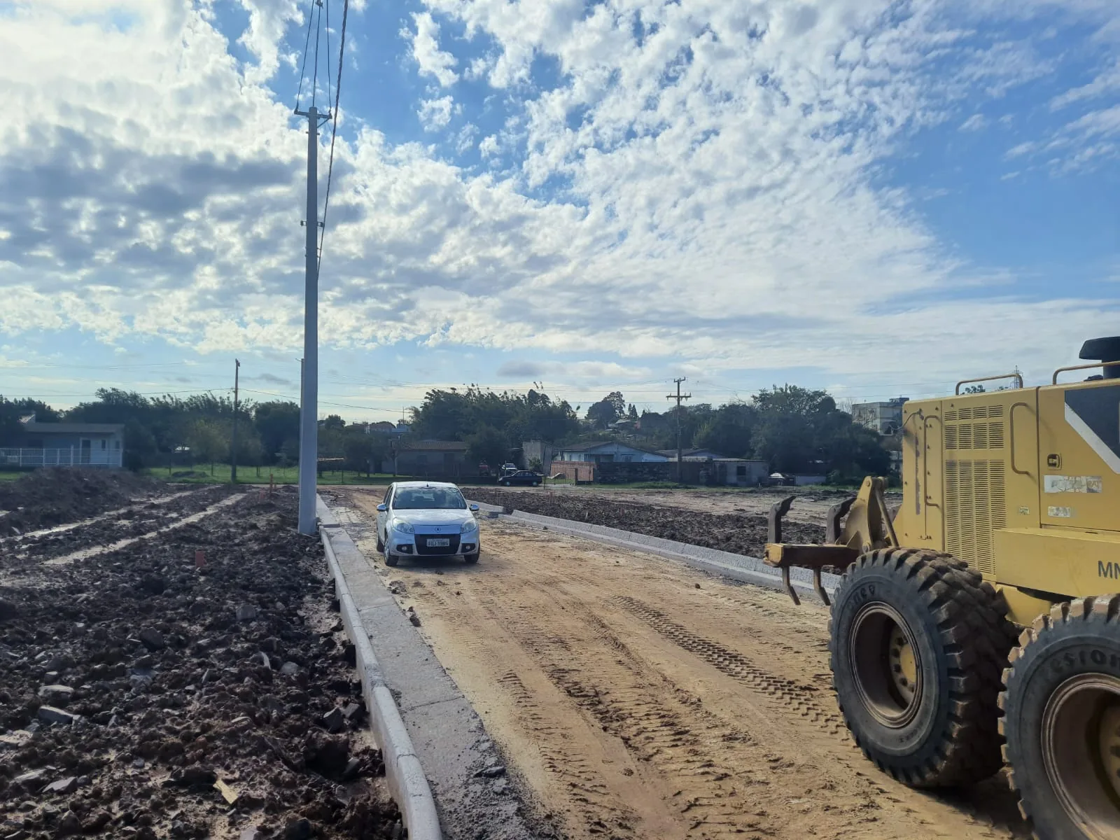 Via em execução com máquina de terraplanagem, iluminação e infraestrutura urbana